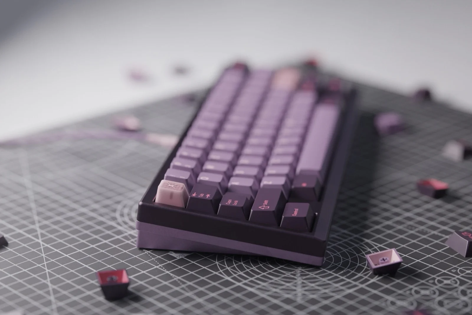 Dark purple 65% keyboard with GMK Symbiote keycaps in deep purple and mauve tones, lighter lavender accent keys, and scattered dark red-purple keycaps on a gray cutting mat
